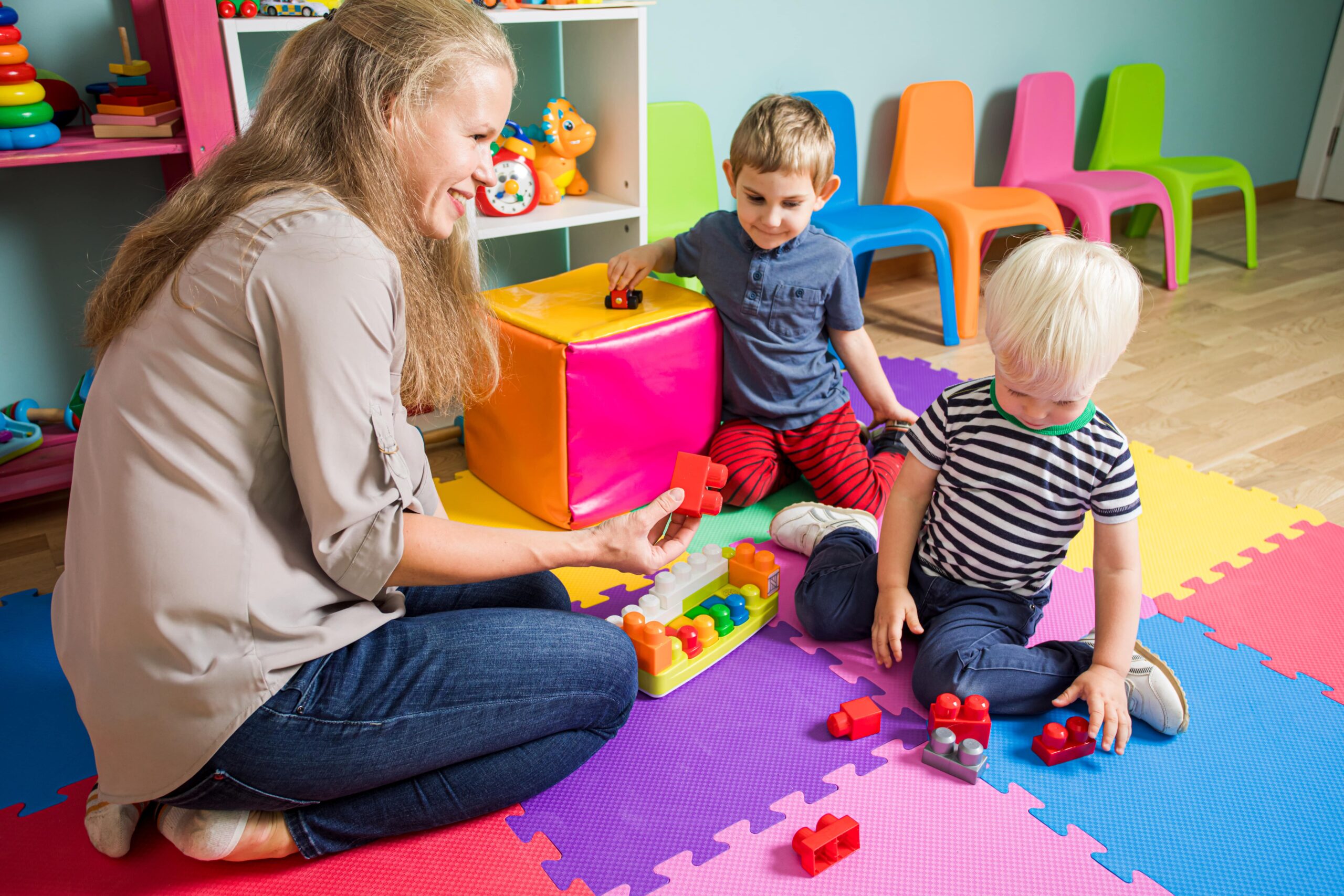 https://doradcy365.pl/wp-content/uploads/2022/04/two-little-boys-are-playing-with-kindergarten-teacher-woman-is-sitting-with-boys-floor-playroom-min-scaled.jpg