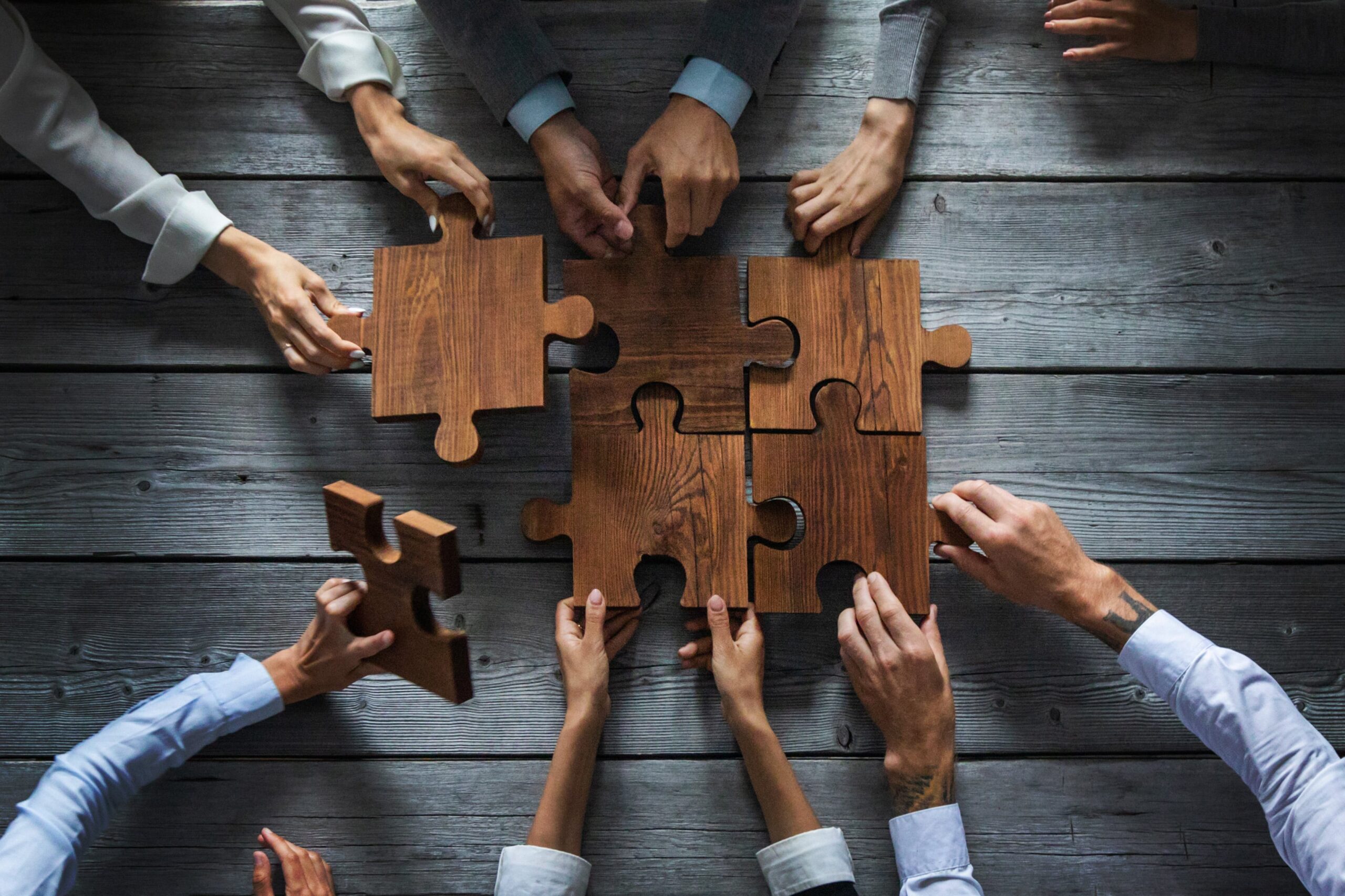 https://doradcy365.pl/wp-content/uploads/2022/12/business-people-team-sitting-around-meeting-table-and-assembling-wooden-jigsaw-puzzle-pieces-unity-cooperation-ideas-concept-min-scaled.jpg